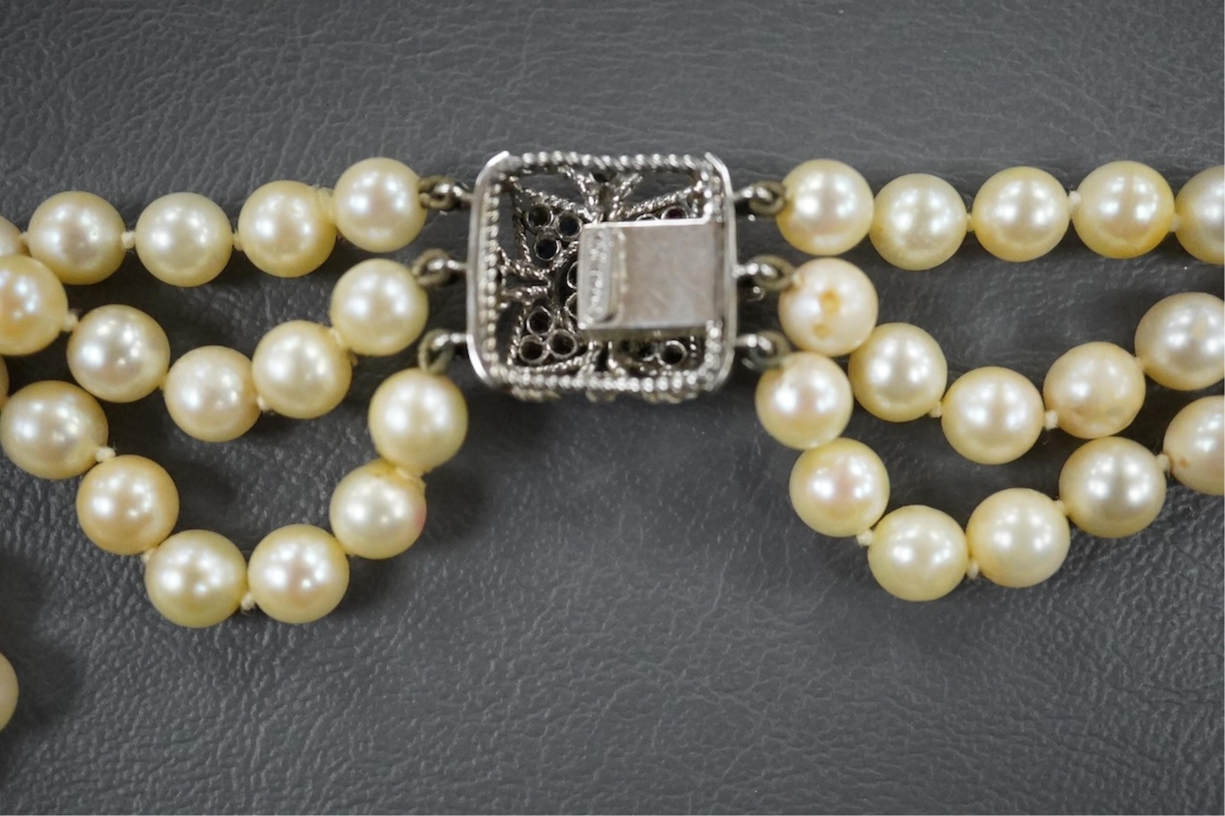 A triple strand cultured pearl necklace, with an Italian 18k white metal, ruby, sapphire and emerald set clasp, 46cm.